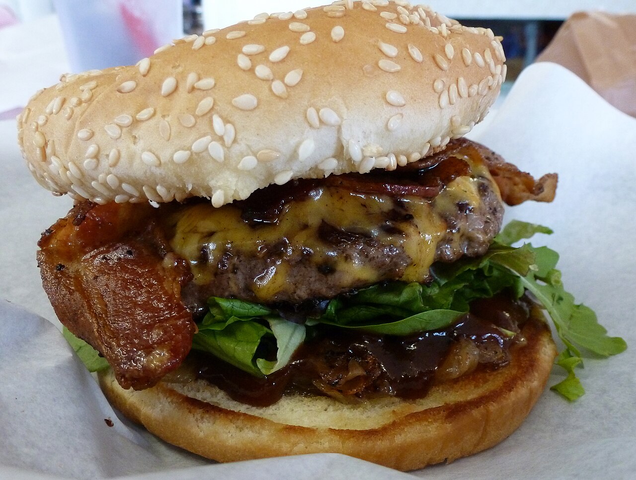 Close-up burger layered with BBQ sauce, bacon, melted cheese, and greens on a toasted bun.